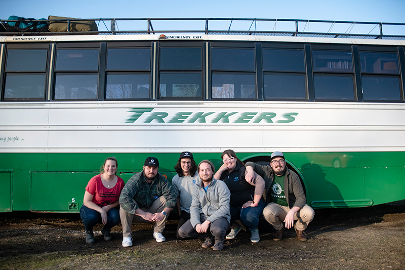 Trekkers Staff gather in front of the green and white Trekkers bus.